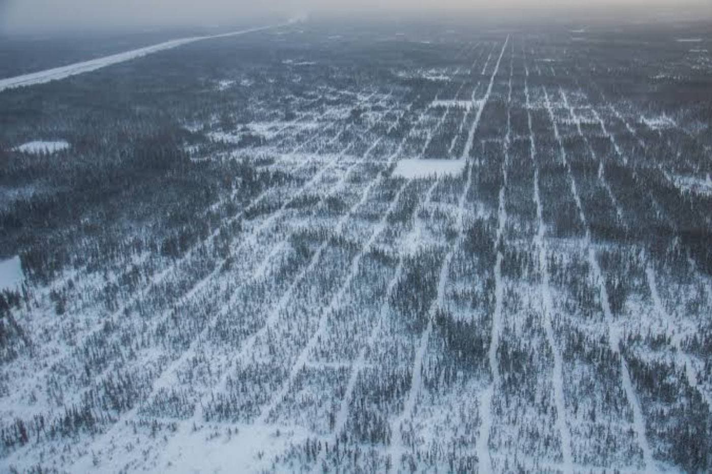 Aerial view of a pumpjack and well pad beside a forested lakeshore